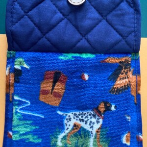 May include: Blue quilted pot holder with a brown button. The front of the pot holder is a blue and white patterned fabric with images of dogs, birds, and trees.