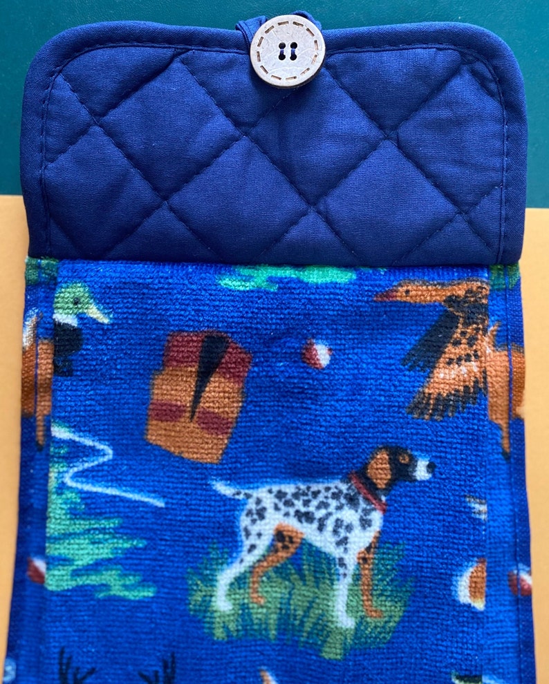May include: Blue quilted pot holder with a brown button. The front of the pot holder is a blue and white patterned fabric with images of dogs, birds, and trees.