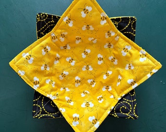 May include: A yellow fabric bowl with a black and yellow trim. The bowl is decorated with a repeating pattern of bees flying around a honeycomb.