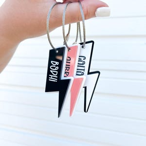 May include: Three black, white, and pink lightning bolt shaped luggage tags with the names "Callie", "Aure", and "Bodhi" written on them.