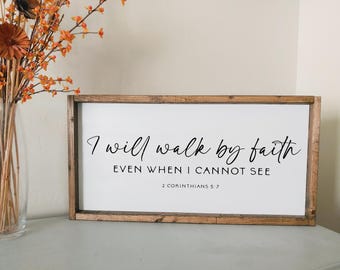 May include: A wooden sign with a white background and brown frame. The sign has black text that reads "I will walk by faith even when I cannot see 2 Corinthians 5:7".
