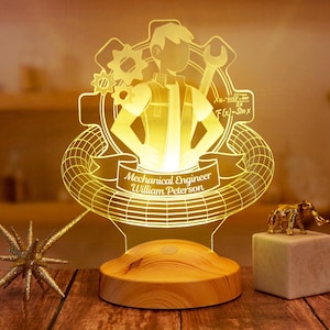 Könnte beinhalten: Ein Holzsockel mit einem 3D-gedruckten Acryllampenschirm, der einen Cartoon-Maschinenbauingenieur mit Zahnrädern und dem Text "Mechanical Engineer William Peterson" zeigt.