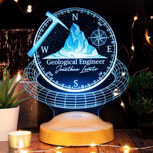 Könnte beinhalten: Ein blaues und weißes 3D-gedrucktes Nachtlicht mit einem Kompass-Design und einer Spitzhacke. Das Nachtlicht trägt den Text "Geological Engineer Jonathan Lovato".