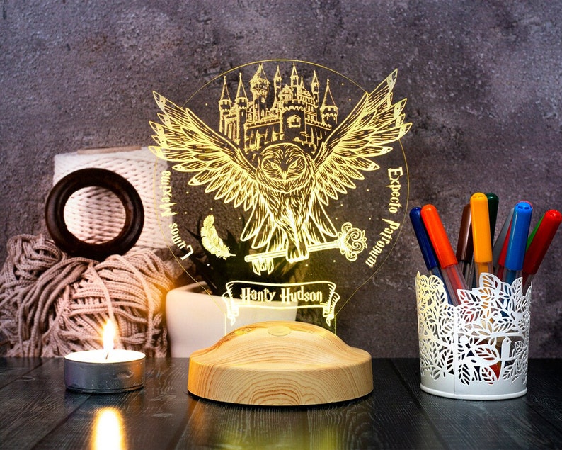 Peut inclure: Une base en bois avec un hibou et un ch&acirc;teau en acrylique imprim&eacute;s en 3D. Le hibou tient une cl&eacute; et le ch&acirc;teau est &eacute;clair&eacute;. Le texte "Expecto Patronum" et "Harry Hudson" sont imprim&eacute;s sur l'acrylique.