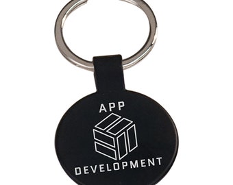 May include: Black round keychain with a silver key ring. The keychain has the words "APP DEVELOPMENT" in white, with a white geometric cube design. The keychain is a promotional item.
