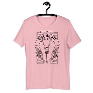 Pu&ograve; includere: T-shirt rosa con un design grafico nero che presenta una mano scheletrica che fa un segno rock and roll con rose e il testo "Ride or Die Till Death Do Us Part".