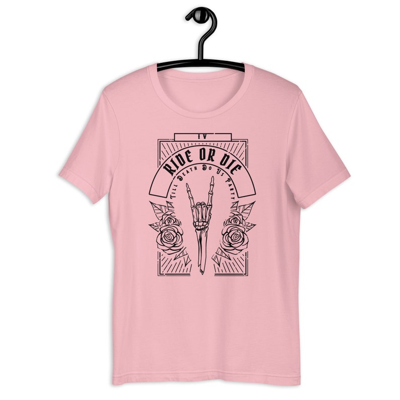 Pu&ograve; includere: T-shirt rosa con un design grafico nero che presenta una mano scheletrica che fa un segno rock and roll con rose e il testo "Ride or Die Till Death Do Us Part".