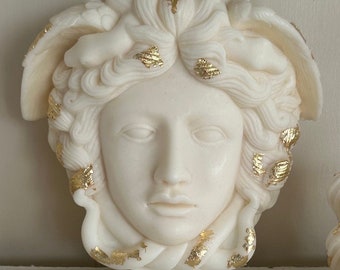 Op de afbeelding: Witte gebeeldhouwde kaars in de vorm van een vrouwenhoofd met accenten van bladgoud. De kaars is een decoratief stuk met een gedetailleerd ontwerp.