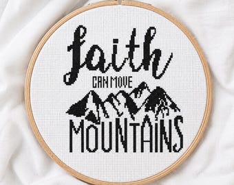 May include: A circular wooden embroidery hoop containing white Aida fabric with a black cross-stitch design. The text reads faith CAN MOVE MOUNTAINS, accompanied by a black stitched mountain range graphic centered between the words.