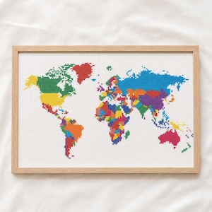 May include: A framed cross-stitch embroidery of a world map on white fabric. The continents are rendered in a vibrant, multi-coloured pixelated style, featuring distinct shades of green, yellow, red, blue, orange, and purple within a light wood frame.