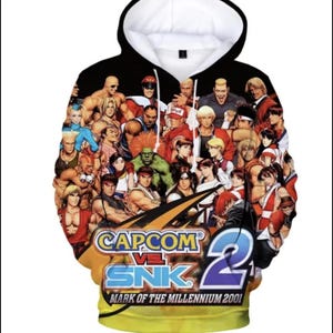 May include: Black hooded sweatshirt featuring a colourful graphic print of characters from the video game Capcom vs. SNK 2: Mark of the Millennium 2001.