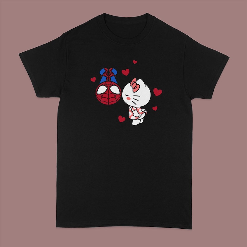 Peut inclure: T-shirt noir avec un imprim&eacute; de Spiderman embrassant Hello Kitty. L'imprim&eacute; est en rouge, blanc et bleu. Il y a de petits c&oelig;urs rouges autour de l'imprim&eacute;.