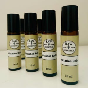 Op de afbeelding: Een aantal amberkleurige glazen roll-on flessen met zwarte doppen. Elke fles heeft een etiket met de tekst "RAW NATURAL SKINCARE COSMETICS" en "Relaxation Roller", en bevat 10 ml.