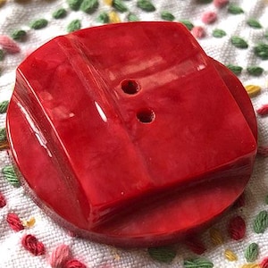 Könnte beinhalten: Ein roter Plastikknopf mit zwei Löchern. Der Knopf hat ein erhabenes, rechteckiges Design.