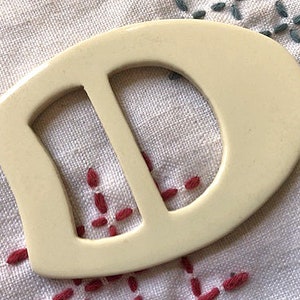 Op de afbeelding: Een witte plastic gesp met een D-vormige opening. De gesp is glad en heeft een matte afwerking.
