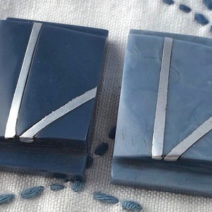 May include: Two rectangular blue and silver decorative tiles with a geometric design. The tiles are made of a smooth, glossy material.
