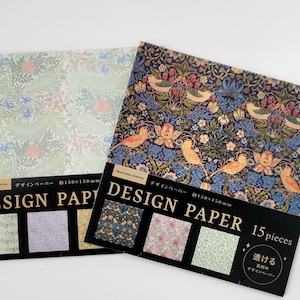 May include: Two packs of design paper with floral and bird patterns. One pack features a light green and pink floral design, while the other showcases a dark blue pattern with birds and flowers. Each pack is labeled "DESIGN PAPER" and includes a variety of sample designs.