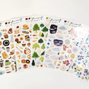Op de afbeelding: Een verzameling sticker vellen met diverse ontwerpen. De vellen bevatten afbeeldingen van koffie, gebak, bomen, wolken, bloemen en een nachtsc&egrave;ne met een maan. Op elk vel staat het woord "Painting Sticker".