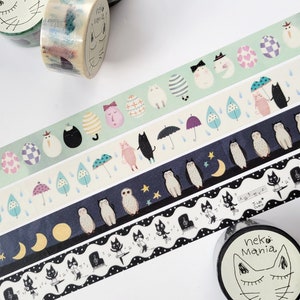 May include: Assortment of washi tapes featuring cute illustrations of cats, owls, eggs, and musical notes. The tapes are on spools with labels that say "Neko Mania".