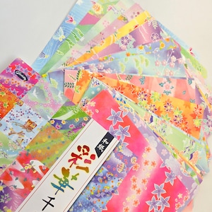 May include: A collection of colorful origami paper sheets with floral and geometric patterns. The papers are in various shades of pink, orange, green, blue, and purple. A package with Japanese text is visible.