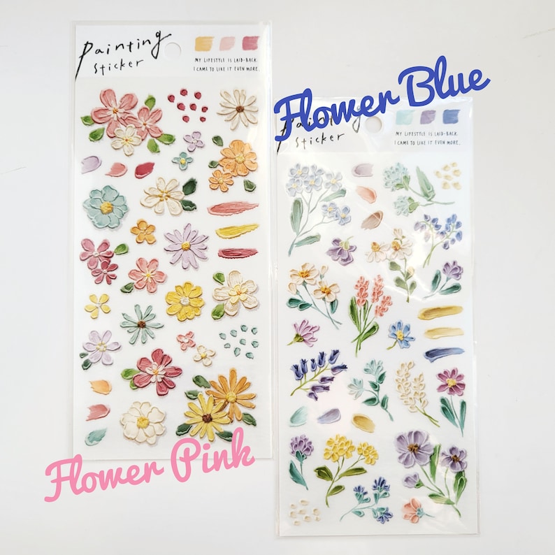 Op de afbeelding: Twee stickervellen met bloemmotieven. E&eacute;n vel is gelabeld "Flower Pink" en bevat roze, gele en oranje bloemen. Het andere vel, "Flower Blue", heeft blauwe, paarse en gele bloemen. Beide vellen zijn gelabeld "Painting Sticker".