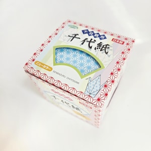 May include: A box of Japanese origami paper, featuring a fan-shaped design with blue and white star patterns. The box has red and white geometric patterns and Japanese text. The text "SENBAZURU CHIYOGAMI" is also visible.
