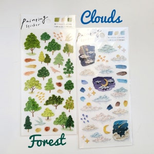 Op de afbeelding: Twee sticker vellen met een bos- en wolken thema. Het bos vel toont groene bomen, een vogel en penseelstreek accenten. Het wolken vel bevat wolken, sterren en een maan. De tekst "Painting sticker" is zichtbaar.