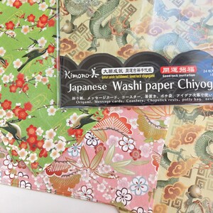 May include: A pack of Japanese Washi paper Chiyogami with four different designs. The designs include a green background with white flowers and birds, a pink background with white flowers and gold accents, a yellow background with a green dragon, and a yellow background with a green dragon and gold accents. The pack includes 24 sheets of paper, each measuring 150mm x 150mm. The text on the pack reads "Kimono 大成運吉祥千代紙 Great wish fulfillment Good luck chayogami 開運招福 Good luck invitation Japanese Washi paper Chiyogami 折り紙、メッセージカード、コースター、箸置き、ポチ袋、アイデア次第で使い方は様々 Origami, Message cards, Coasters, Chopstick rests, potty bag, next idea"