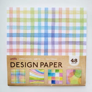 May include: A pack of 48 watercolor design papers with 4 different patterns. The patterns include a checkered pattern, a rainbow stripe pattern, a colorful square pattern, and a pattern of overlapping circles. The pack is labeled "amifa Design Paper Watercolor Pattern 150x150mm".