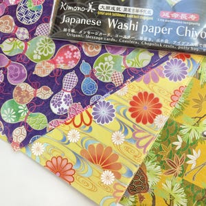 May include: Three sheets of Japanese Washi paper with different patterns. The first sheet has a purple background with colorful gourds. The second sheet has a yellow background with red, orange, and white flowers. The third sheet has a yellow background with a green and white crane and pine trees.