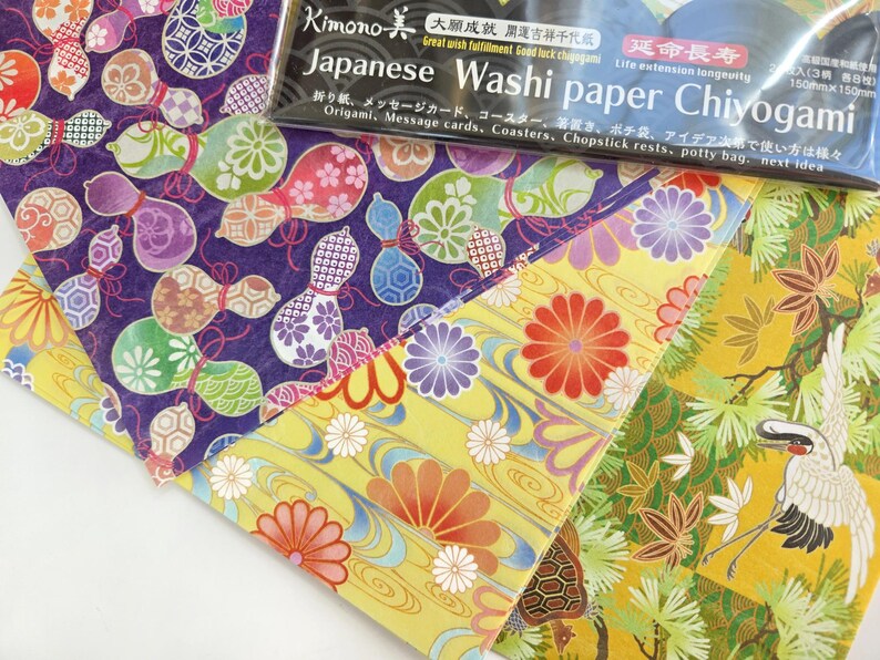 May include: Three sheets of Japanese Washi paper with different patterns. The first sheet has a purple background with colorful gourds. The second sheet has a yellow background with red, orange, and white flowers. The third sheet has a yellow background with a green and white crane and pine trees.
