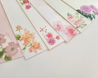 Op de afbeelding: Vijf verschillende bloemige briefkaarten met roze, witte en oranje bloemen. De kaarten zijn in een waaier gerangschikt, met de bovenste kaart die een paarse bloem laat zien.