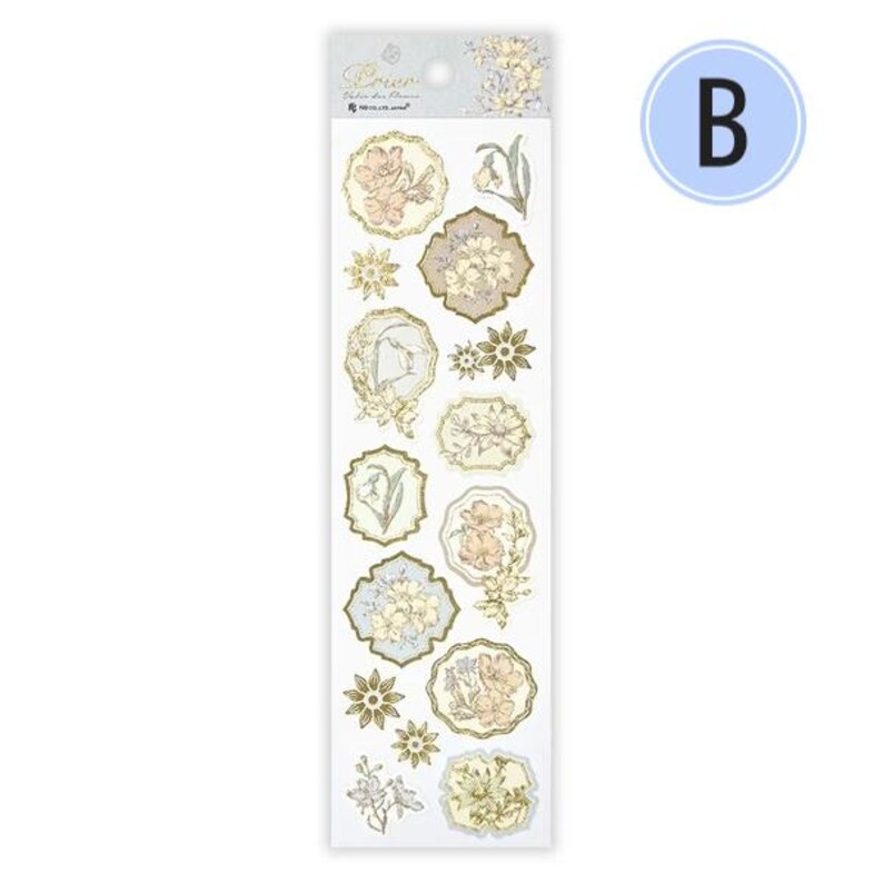 Op de afbeelding: Een vel decoratieve stickers met bloemmotieven in pastelkleuren. De stickers bevatten verschillende vormen en maten, met goudfolie accenten. Het vel heeft een lichtblauwe en witte achtergrond met de letter "B" in een blauwe cirkel.