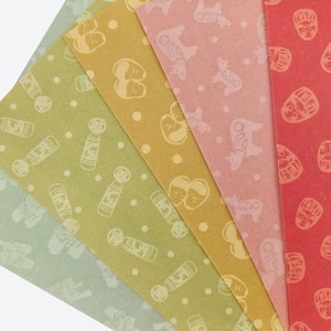 May include: A selection of patterned paper sheets in a fan arrangement. The sheets display various designs in shades of green, yellow, pink, and red. Patterns include dolls, animals, and other shapes. The paper has a slightly textured finish.