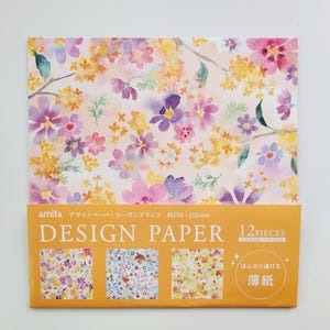 May include: A pack of 12 floral design papers with a watercolor look. The papers are approximately 6 inches by 6 inches and feature a variety of pink, purple, and yellow flowers on a white background. The pack includes the text "Design Paper" and "12 Pieces".