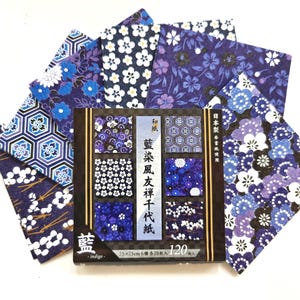 May include: A set of 120 sheets of indigo-colored decorative paper featuring various floral and geometric patterns. The packaging displays the text 藍, indigo, and 25x75cm 6種 各20枚入 120枚入. The paper sheets are arranged in a fan shape behind the box.