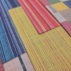 May include: Close-up of colorful fabric samples with various striped and patterned designs. The fabrics feature a mix of colors, including blue, red, yellow, and multi-colored stripes, showcasing a variety of textures and patterns.