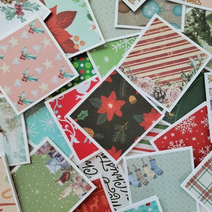 May include: A collection of square Christmas-themed paper cards with various patterns. Designs include poinsettias, snowflakes, holly, stripes, and reindeer. The cards have white borders and are arranged in a scattered, overlapping manner.
