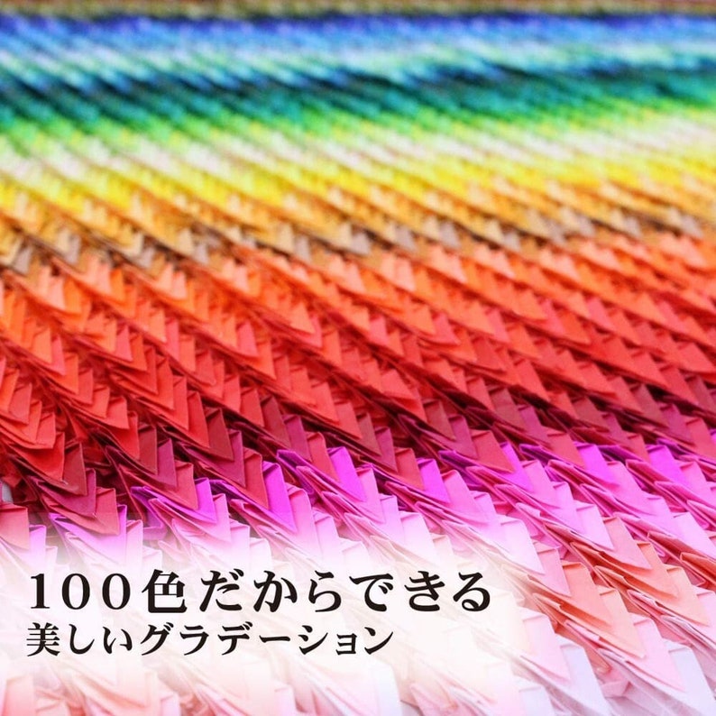 May include: A close-up of a colourful, layered paper art piece. The artwork features a gradient of colours, transitioning from blue to red, with Japanese text. The text reads "100 colours can do it" and "beautiful gradation".