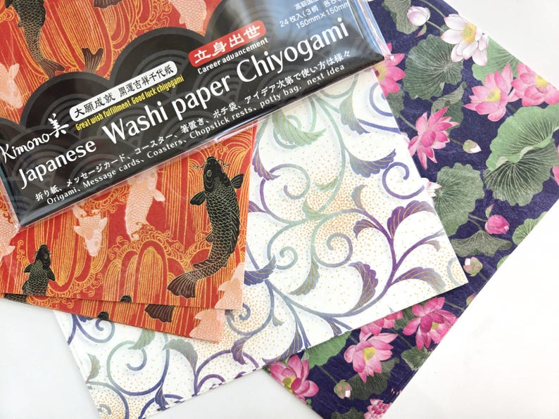 May include: A pack of Japanese Washi paper Chiyogami, with a black background and white text. The text reads "Japanese Washi paper Chiyogami" and "Career advancement". The pack contains three sheets of paper with different designs: one with red and gold koi fish, one with white and gold floral designs, and one with blue and green lotus flowers.