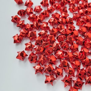 May include: A large group of red origami lucky stars scattered on a white surface. The stars are made of shiny paper and have a metallic sheen.