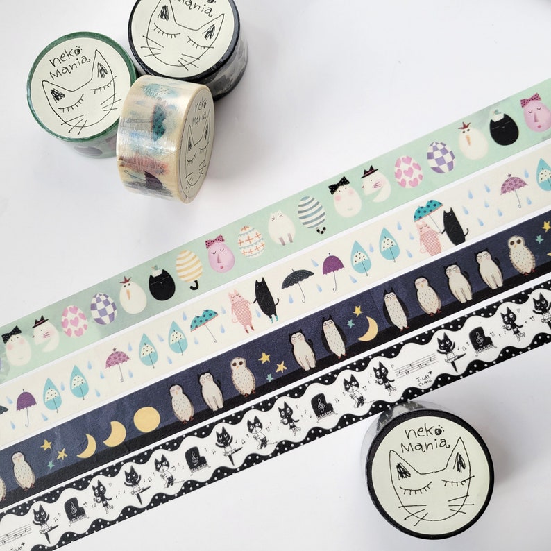 May include: Assortment of washi tapes featuring cute illustrations of cats, owls, eggs, and musical notes. The tapes are on spools with labels that say "Neko Mania".