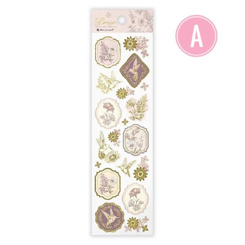 Op de afbeelding: Een vel decoratieve stickers met bloemen- en kolibrie-ontwerpen in roze, goud en paars. De stickers hebben een vintage esthetiek, met sierlijke frames en delicate illustraties. Het woord "Dorie" staat bovenaan gedrukt.