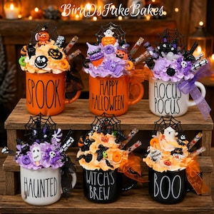 May include: Six ceramic mugs with Halloween-themed faux whipped cream toppings, featuring text like SPOOK, HAPPY HALLOWEEN, HOCUS POCUS, HAUNTED, WITCH'S BREW, and BOO. Each mug is decorated with miniature plastic spiders, webs, and ghosts.