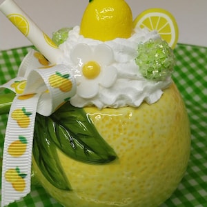 May include: A yellow ceramic mug shaped like a lemon, decorated with a white whipped cream topping, a lemon slice, and a whole lemon. A white ribbon with lemon designs and a straw with lemon slices are also included. The text "BirdDsFakeBakes" is at the bottom.