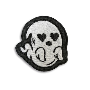 May include: A black and white embroidered patch of a ghost with heart-shaped eyes. The ghost is smiling and has a small black nose.