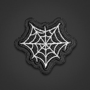 Puede incluir: Un parche bordado en blanco y negro con un diseño de telaraña. El parche tiene un borde negro grueso y un patrón de telaraña blanco central cosido sobre una base de tela negra, creando un contraste marcado entre los hilos oscuros y claros.