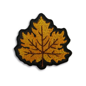 Könnte beinhalten: Ein gestickter Ahornblattflicken in Gelb auf schwarzem Stoff.
