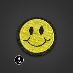 Könnte beinhalten: Ein kreisförmiger, bestickter Aufnäher mit einem leuchtend gelben Smiley-Gesicht, schwarzen gestickten Augen und einem geschwungenen Mund. Der Aufnäher hat einen dicken schwarzen Rand. Ein kleines weißes Symbol zeigt den Text 3 PCS in Schwarz.