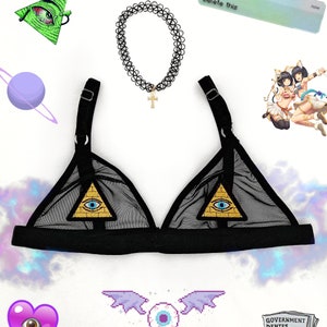 Könnte beinhalten: Schwarzes Mesh-Bralette mit verstellbaren Trägern und goldgestickten Eye-of-Providence-Patches. Das Bild enthält auch eine schwarze Choker-Halskette mit einem goldenen Kreuzanhänger und weitere grafische Elemente.